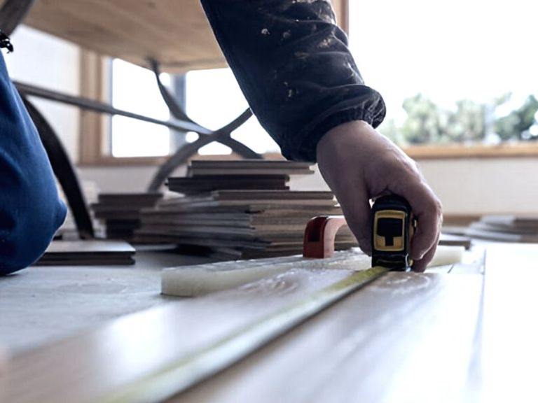 Handwerker misst eine Diele an, daneben liegt der vorbereitete Belag
